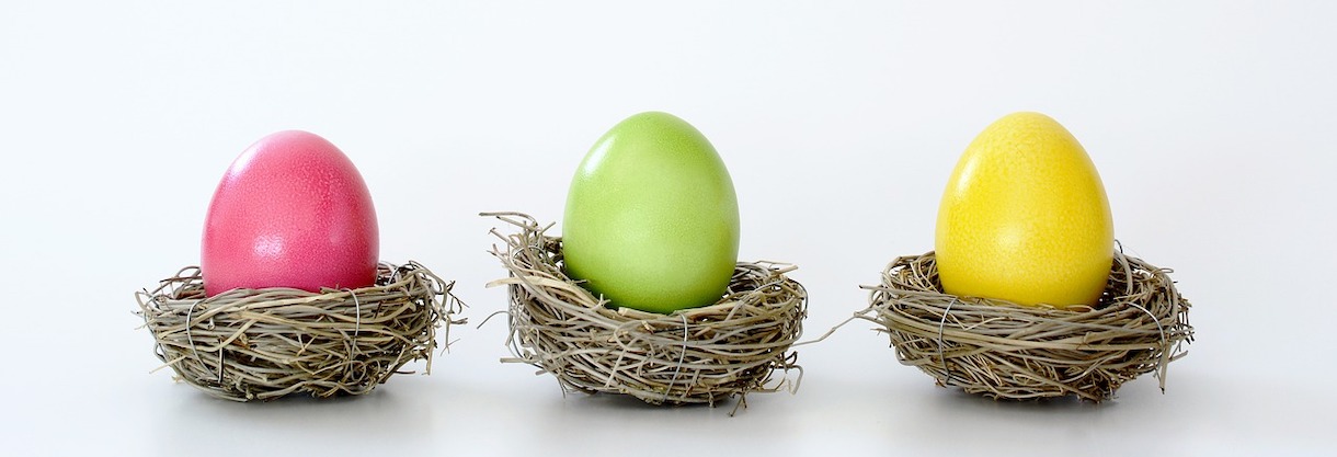 Pink, yellow, and green dyed eggs sit in their own individual small nests.
