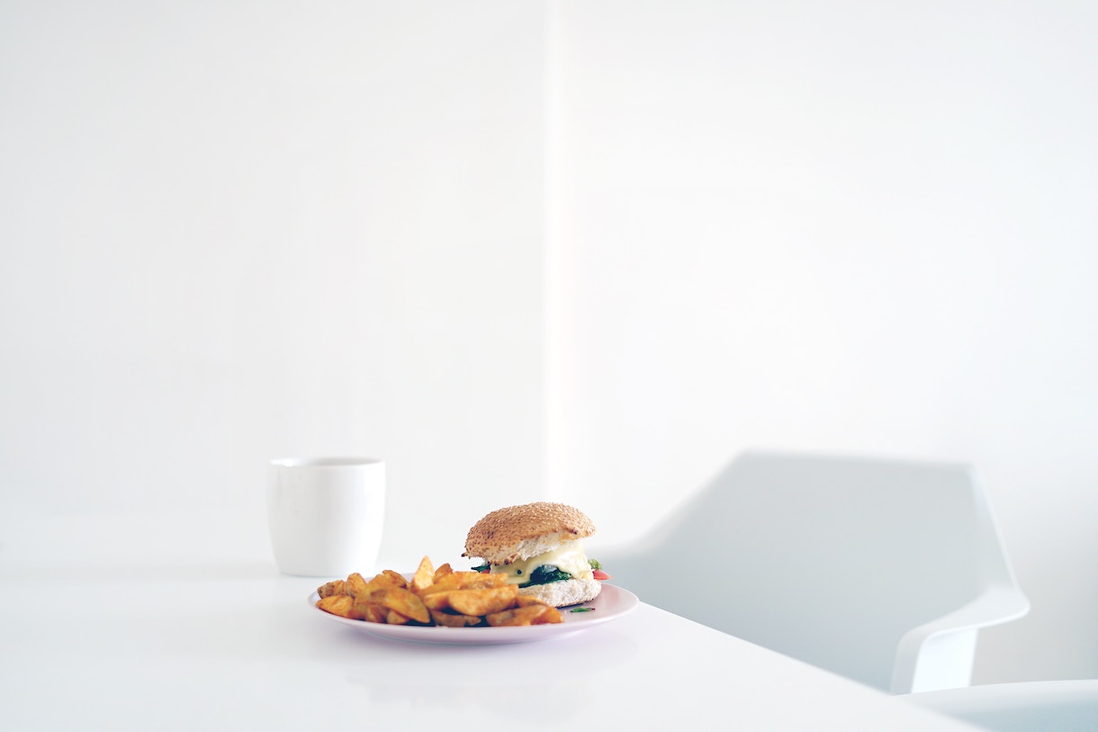 A burger on a white plate on a large white table