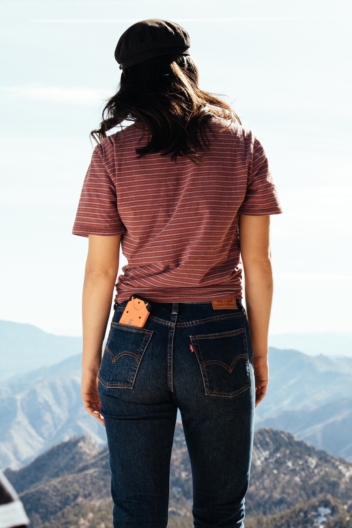 iPhone sticking half way out of back pocket of jeans, while woman looks at mountains in distance