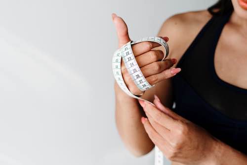 Woman in black sports bra wraps measuring tape around her hand.